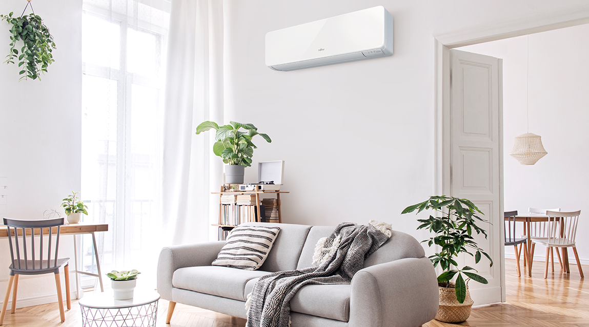 Bright and airy living room with a wall-mounted energy-efficient air conditioner. Designed for comfort, it features natural light, indoor plants, and well-arranged furniture to enhance airflow, reduce energy use, and create a sustainable, cosy atmosphere.